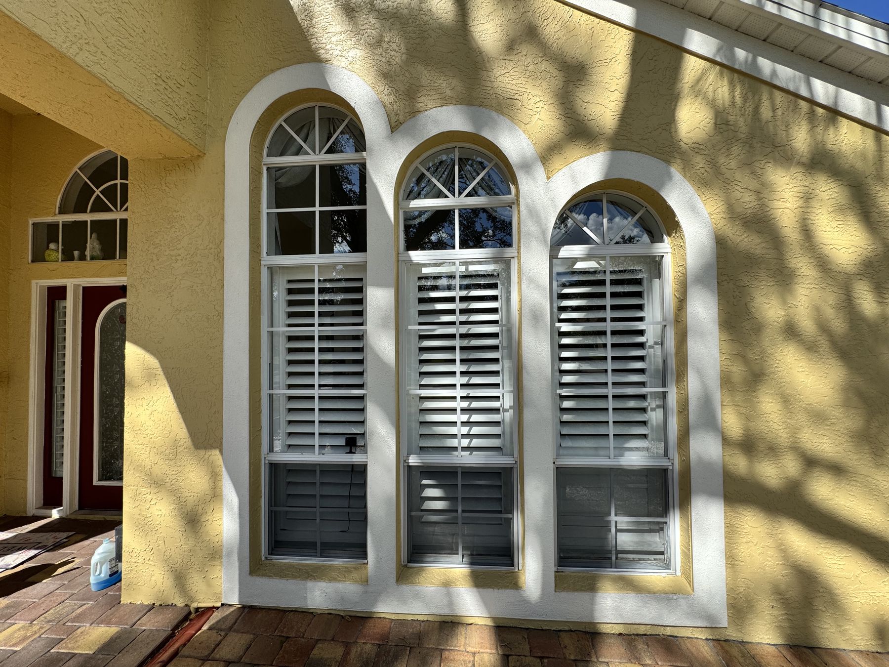 Three arched windows with plantation shutters on a yellow stucco home